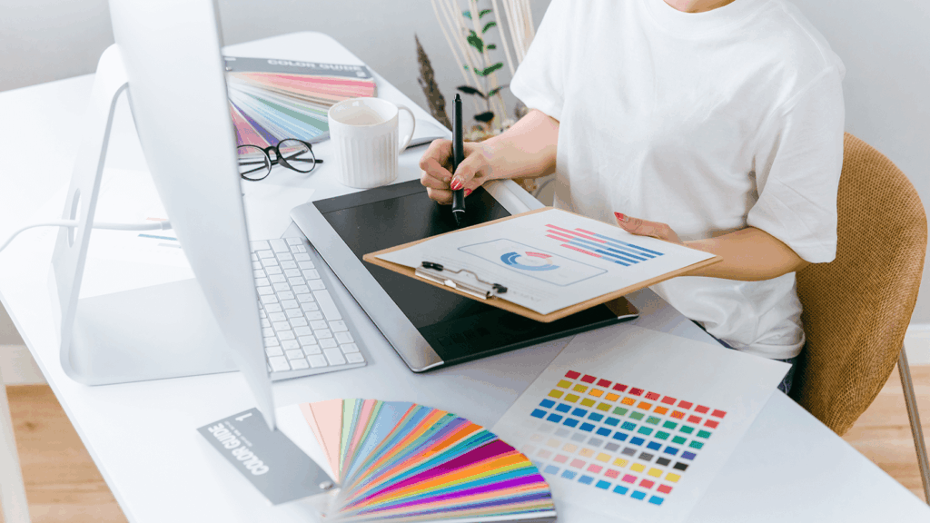 デザイナーがペンタブで作業しながら、配色チャートを確認している写真。